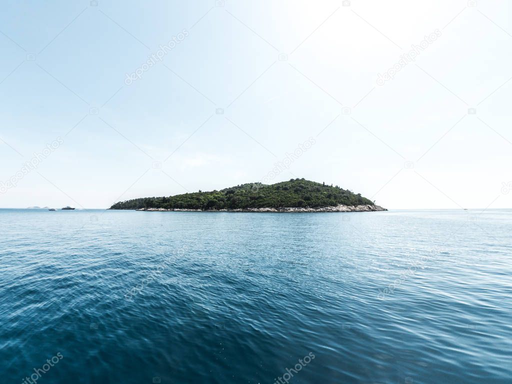Beautiful panoramic view of the tree covered island of Lokrum in the Adriatic Sea in Croatia with blue sky above and water below.