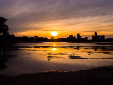 Güzel, parlak, doymuş ve canlı günbatımı turuncu, sarı, mavi ve mor renkli bulutlar yağmur su birikintileri Chicago Illinois Montrose plajda kuma yansıtan yukarıda gökyüzünde ile.