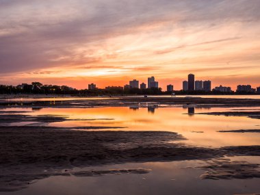 Yağmur su birikintileri Chicago Illinois Montrose plajda kuma yansıtan yukarıda gökyüzünde renkli turuncu, sarı ve mor bulutlar ile yangın Sunset'teki muhteşem boyalı gökyüzü.