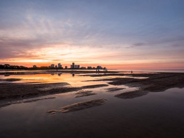 Güzel, parlak, doymuş ve canlı günbatımı turuncu, pembe, mavi ve mor renkli bulutlar yağmur su birikintileri Chicago Illinois Montrose plajda kuma yansıtan yukarıda gökyüzünde ile.