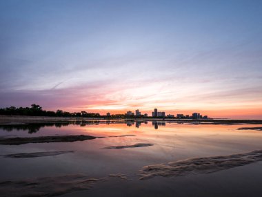 Güzel, parlak, doymuş ve canlı günbatımı turuncu, pembe, mavi ve mor renkli bulutlar yağmur su birikintileri Chicago Illinois Montrose plajda kuma yansıtan yukarıda gökyüzünde ile.