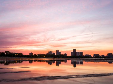 Güzel, parlak, doymuş ve canlı günbatımı turuncu, pembe, mavi ve mor renkli bulutlar yağmur su birikintileri Chicago Illinois Montrose plajda kuma yansıtan yukarıda gökyüzünde ile.