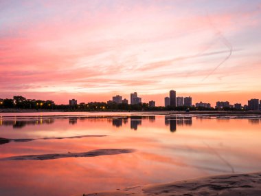 Güzel, parlak, doymuş ve canlı günbatımı turuncu, pembe, mavi ve mor renkli bulutlar yağmur su birikintileri Chicago Illinois Montrose plajda kuma yansıtan yukarıda gökyüzünde ile.