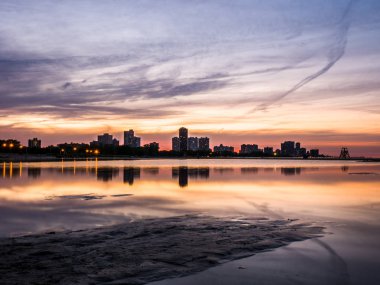 Güzel, parlak, doymuş ve canlı günbatımı turuncu, pembe, mavi ve mor renkli bulutlar yağmur su birikintileri Chicago Illinois Montrose plajda kuma yansıtan yukarıda gökyüzünde ile.