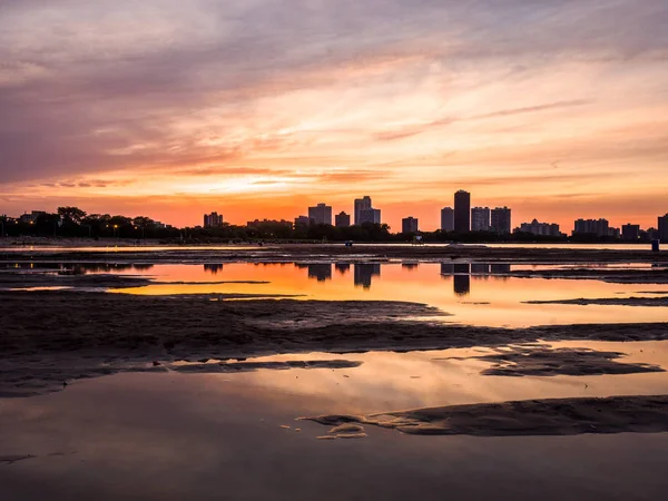 Yağmur su birikintileri Chicago Illinois Montrose plajda kuma yansıtan yukarıda gökyüzünde renkli turuncu, sarı ve mor bulutlar ile yangın Sunset'teki muhteşem boyalı gökyüzü.
