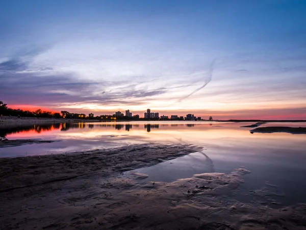 Güzel, parlak, doymuş ve canlı günbatımı turuncu, pembe, mavi ve mor renkli bulutlar yağmur su birikintileri Chicago Illinois Montrose plajda kuma yansıtan yukarıda gökyüzünde ile.