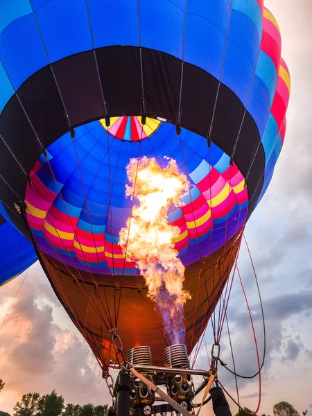 A close up photograph looking up inside a hot air balloon as a ball of fire or flames shoot upward into the colorful balloon with dramatic clouds at sunset beyond in Galena Illinois.