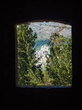 Yaprak dökmeyen ağaçlar çerçeveleme Lokrum Adası üzerinde manzara ile Adriyatik Denizi ve yamaç evler Dubrovnik Hırvatistan mavi sularına açılan kemerli bir üst dışarı güzel tatil fotoğraf.