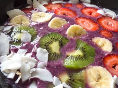 Görünümü bir canlı ve taze meyve acai kase veya mor renkli blueberry smoothie çilek, muz, kivi güler yüzlü kase tepesinde ve Hindistan cevizi siyah kase astar pul.