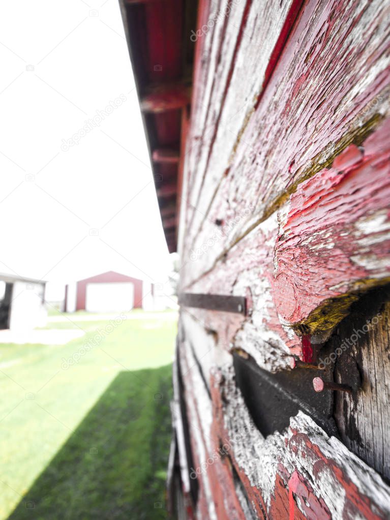 Close-up photograph of the side of a weathered wood barn with red paint pealing off of old grey colored wood siding with rusted nails and pieces missing.