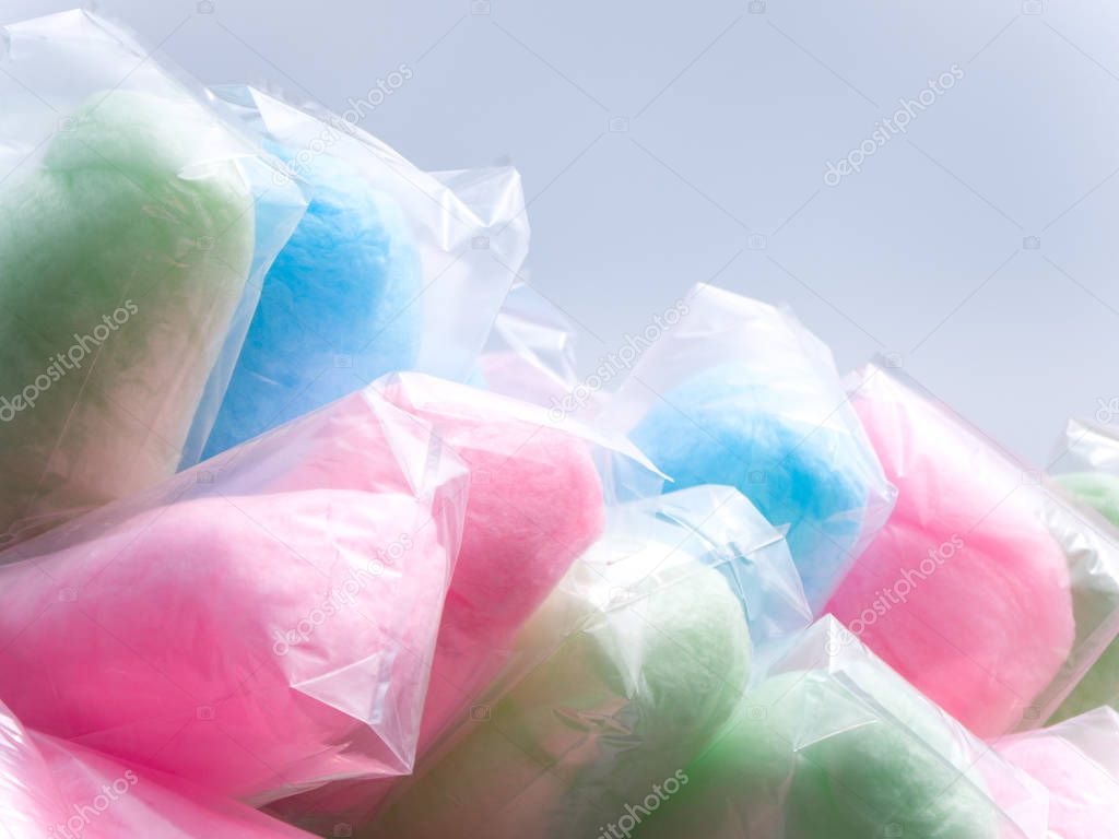 Colorful bags full of cotton candy including green, pink, blue and purple on a street vendor stick during an event with gray sky beyond.