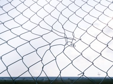 Bir bükülmüş chainlink çit ve zarar center ve ötesinde bulutlu gökyüzü portre fotoğrafı.