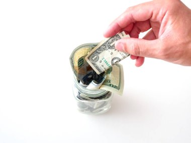 Beyaz bir beyaz erkek nakit para ile taşan bir cam kavanoza mason tasarruf bir dolarlık banknot koyarak el ve beyaz bir arka plan üzerinde izole.