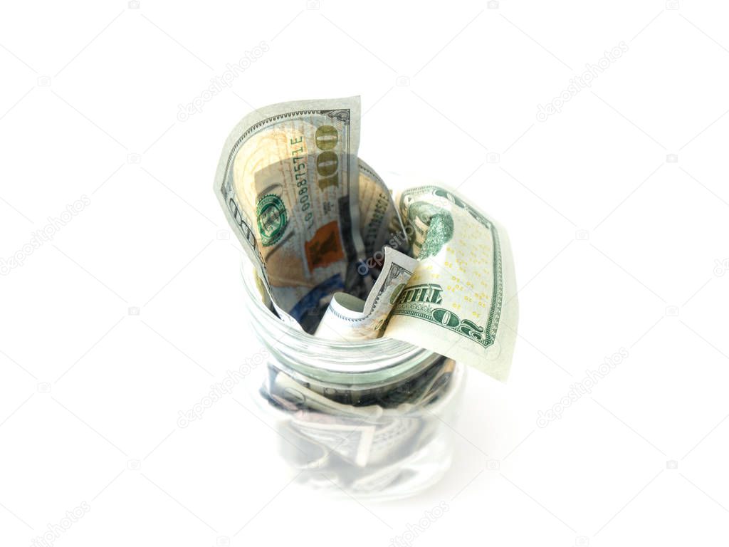 A view of a glass mason savings jar full of cash stuffed inside including singles, twenties and hundred dollar bills isolated on a white background.