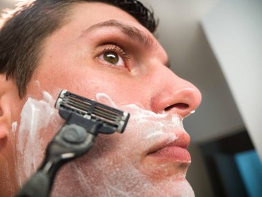 Yüzünü tıraş kremi ile onun sakalı, boyun ve bıyık alanı kapsayan tıraş hazırlanırken beyaz beyaz erkek aynaya bakar.