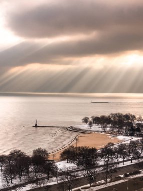 Chicago, Il - 28th Kasım 2018: kar yere oturur gibi dramatik sarı güneş ışınları ile cumulus bulutları bir boşlukta Michigan Gölü su ve kıyı beslemek beach yakınındaki kışın parlaklık.