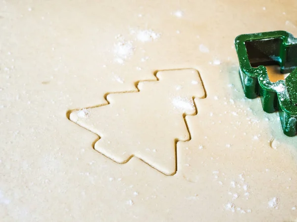 A closeup of a Christmas tree cutout in sugar cookie dough with flour and green plastic stencil or cookie cutter laying on top of dough making a festive background image for the holidays.