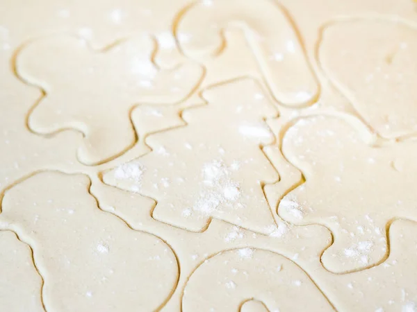 A closeup of a Christmas tree cutout and other holiday stencils or shapes including gingerbread man cut in raw sugar cookie dough with flour sprinkled on top making a beautiful festive background.