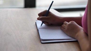 Bir ahşap yemek masada oturan ve onun kağıt notepad ile elleri ve çerçeve göğsünden bir kalemle not yazma pembe gömlek giymiş bir siyah karışık yarış Afrikalı-Amerikalı kadın portre görünümünü.