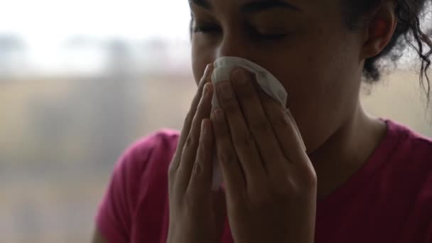 Un primer plano de una mujer afroamericana de raza mixta negra que lleva una camisa rosa mientras se sopla la nariz con un pañuelo y la limpia de una enfermedad o una enfermedad de resfriado común. . — Vídeos de Stock