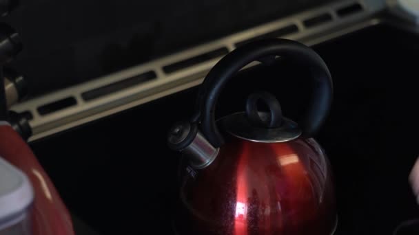 Primer plano de una mujer afroamericana que lleva una camisa rosa mientras vierte agua caliente y humeante de un hervidor de té rojo brillante usado con mango negro redondo y pico de cromo en una taza de cerámica negra con bolsa de té . — Vídeo de stock