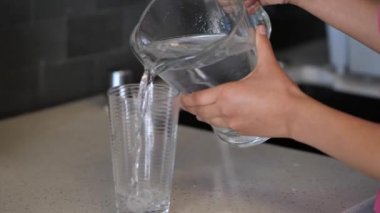 Bir karışık etnik köken Afrika Amerikan kadın bir cam bardak içine mutfak lavabo yakın bir karşı bir cam sürahi su dökme yakın.