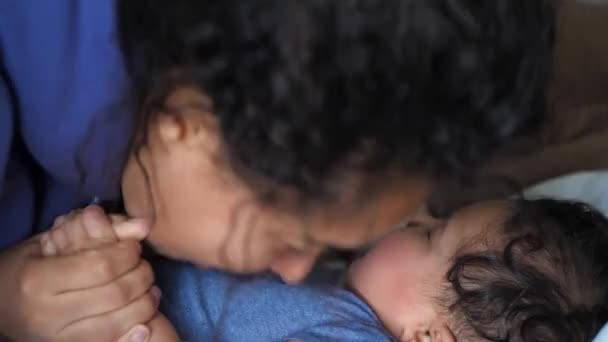 Um close-up de uma mista mãe afro-americana como ela beija e mordisca em seu bebê gordinho saudável deitado na cama como eles fazem ruídos brincalhões para o outro . — Vídeo de Stock