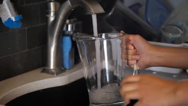 Um close-up de uma etnia mista afro-americana enchendo água da torneira em um jarro de vidro da pia da cozinha . — Vídeo de Stock