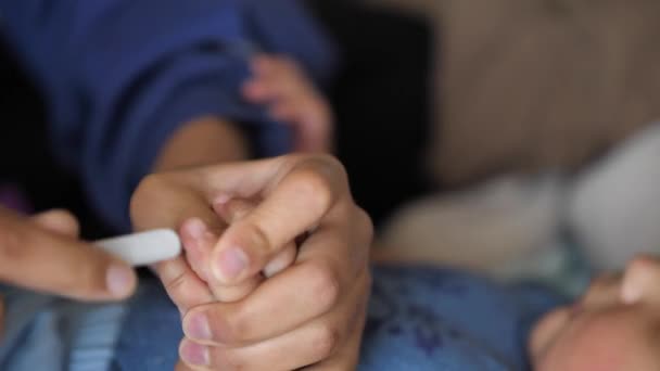 Un gros plan d'une mère métisse classant les ongles de son bébé zoomait et se concentrait sur leurs mains avec bébé flou en arrière-plan et se tortille et se tortille quand elle finit . — Video