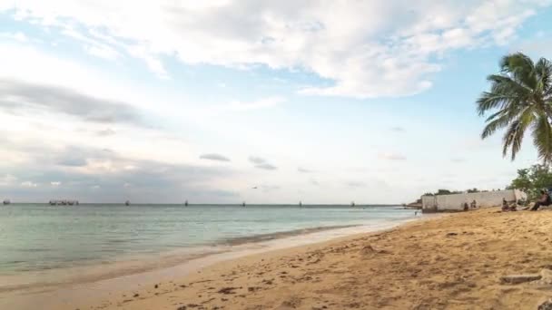 Montego Bay, Jamaica - 23 de marzo de 2019: Turistas y lugareños disfrutan de una hermosa velada descansando en la arena y nadando en el tranquilo agua en la playa Deadend Buccaneer antes del atardecer mientras las nubes pasan por encima . — Vídeos de Stock