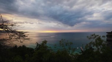 Ön planda ağaçlar ile Karayip Denizi Jamaika adasında Montego Körfezi'nde Atlantik Okyanusu üzerinde gökyüzünde pembe, turuncu ve mavi bulutlar ile güzel bir gün batımı bir el dikey tava