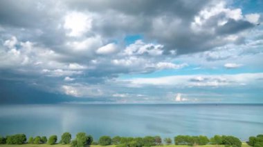 Mavi gökyüzünde beyaz kabarık bulutların Ariel timelapse Aşağıda kıyı şeridi boyunca yeşil ağaçlar ve Chicago'da mesafe ufuk ile Michigan Gölü'nün su üzerinde haddeleme.