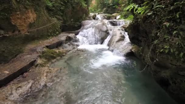 Uma vista espetacular sobre o rio de cachoeiras em cascata e piscinas naturais tropicais na bela atração turística Cool Blue Hole em Ocho Rios Jamaica com vegetação exuberante que reveste o rio — Vídeo de Stock