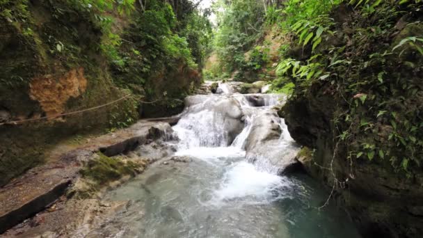 A slow motion view looking up the river of cascading waterfalls and tropical natural pools at the beautiful Cool Blue Hole tourist attraction in Ocho Rios Jamaica with lush vegetation lining the river — Stock Video