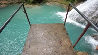 Yavaş hareket atlama platformu kenarına yürüme ve ocho Rios Jamaika güzel Cool Blue Hole şelale ve doğal havuzları aşağıda popüler eğimli şelale ve yüzme havuzu aşağı bakarak.