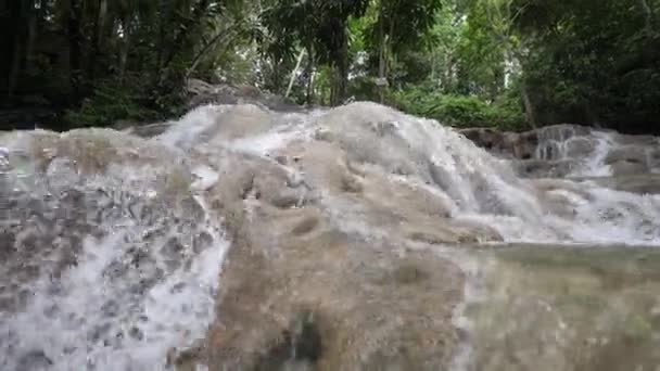 Slow Motion low Vantage Point-weergave van de trapsgewijze watervallen bij Dunn's River Falls met weelderige vegetatie met water spatten in Ocho Rios op tropisch eiland Jamaica een populaire reisbestemming. — Stockvideo