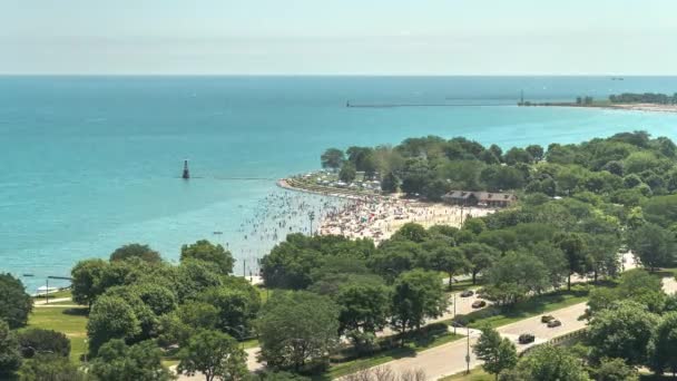 シカゴ、イル - 2019年7月4日:ミシガン湖のビーチで飛行機、ボート、車が転がり、群衆が砂と近くの公園を詰め込み、暑い夏の天気を楽しむために日光浴をします。. — ストック動画