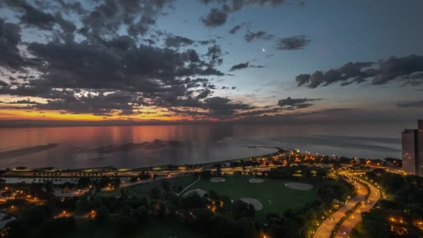 Chicago, Il-29 juni 2019: månen rör sig över moln i en färgstark himmel som trafiken börjar plocka upp nära North Avenue som solen kommer upp över horisonten och stadens ljus bleknar i Lincoln Park. — Stockvideo