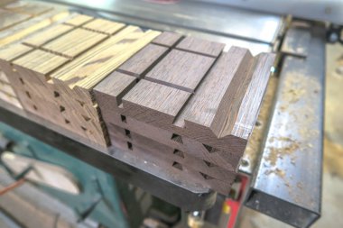 Bir masa testere üzerinde oturan bir ahşap projesi için çeşitli işlenmiş kesim ve oluklar ile egzotik ahşap yığılmış ve sıralanmış üretim parçaları closeup.