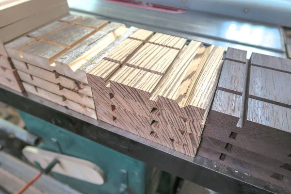 Closeup of stacked and sorted production pieces of exotic wood with various machined cuts and grooves for a woodworking project sitting on a table saw.