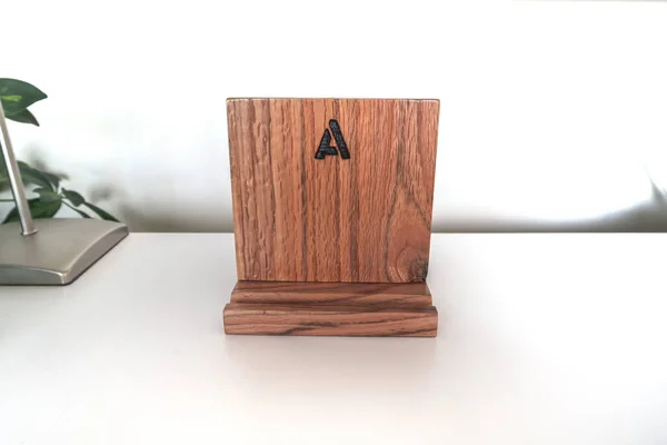 Close up photograph of a handmade homemade cell phone landing pad with wallet and key storage with the letter A engraved on the face made of aged recycled oak wood.