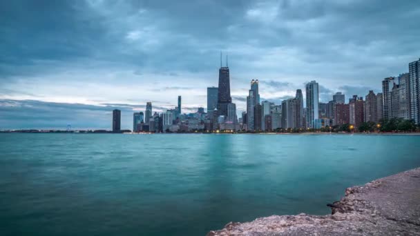 Lapso de tiempo del centro de Chicago a través del lago Michigan como se ve desde la playa de North Avenue con nubes que se mueven a través del cielo nublado por encima de la anochecer se convierte en noche y las luces de la ciudad se encienden. — Vídeo de stock