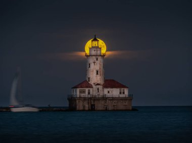 Yelkenli karanlık su üzerinde geçerken Chicago Michigan Gölü boyunca terk edilmiş tarihi ışık ev kulesinin merkezi ile hizalar gibi hasat dolunay güzel bir gece çekimi.