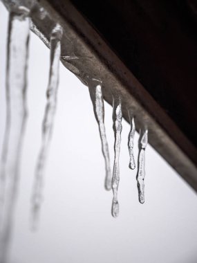 Birkaç dondurulmuş buz sarkıtları beyaz bulutlu arka plan ile kışın soffit kenarında bir çatı fasya kurulu asmak.