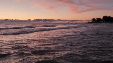 Gorgeous panoramic landscape view of a colorful blue pink and purple sunrise over the water of Lake Michigan as waves gently roll in to the shoreline with clouds on the horizon.