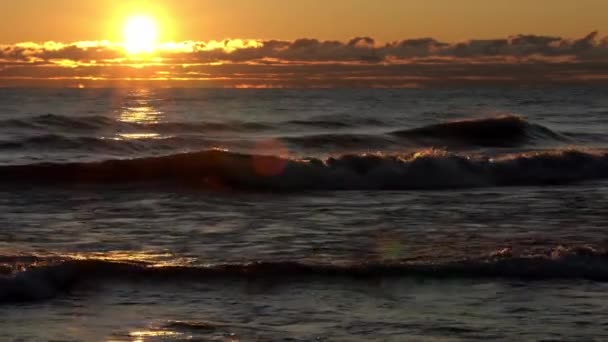 Nádherná pánev s rozptylovým sklem, jak slunce vychází nad mraky na obzoru a odráží zlaté světlo na vlnách na jezeře. — Stock video