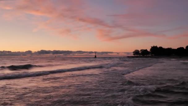 Magnífica vista panorámica del paisaje de un colorido rosa azul y púrpura amanecer sobre el agua del lago Michigan como olas suavemente rodar en la costa con nubes en el horizonte . — Vídeos de Stock