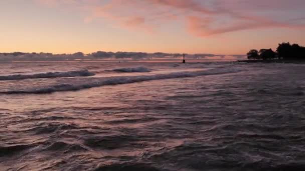 Gorgeous panoramic landscape view of a colorful blue pink and purple sunrise over the water of Lake Michigan as waves gently roll in to the shoreline with clouds on the horizon. — Wideo stockowe