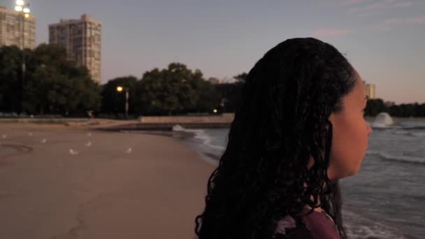 Michigan Gölü kıyısında bir plajda duran güzel bir Afro-Amerikan melez kadının 360 daire şeklindeki manzarasını kapatın ve dalgalar içeri girerken güneşin doğuşunu seyredin.. — Stok video