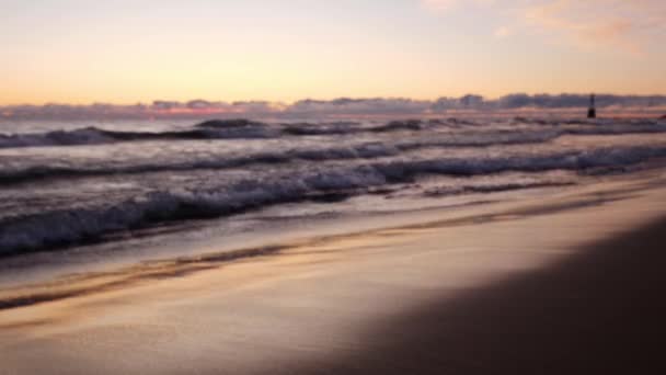 Brak ostrości tło ujęcie fal toczących się do piaszczystej linii brzegowej plaży z kolorowym różowym fioletowym i niebieskim słońcem niebo odbija się na mokrym piasku i wodzie. — Wideo stockowe